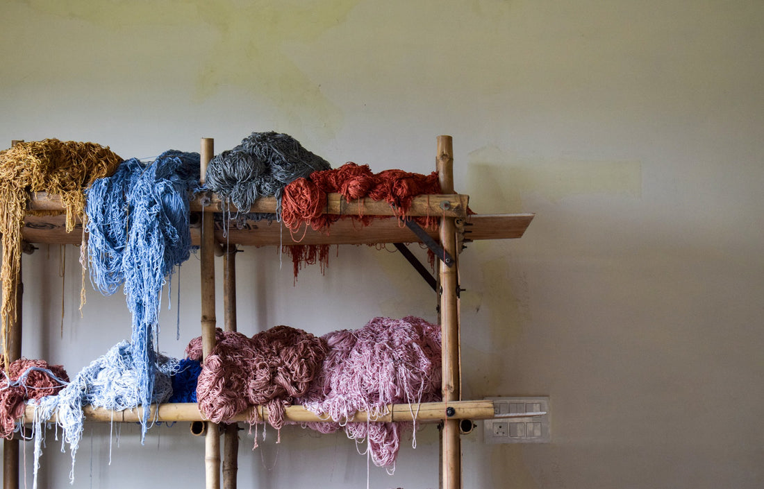 Bunches of naturally dyed yarn in blue, green and purple on a wooden shelf in an artisan workshop in Gwalior, Madhya Pradesh, evoking the natural-dye colour palette behind India's hand block printing tradition