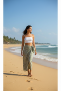 Woman walking on a beach wearing a white top and green sarong.