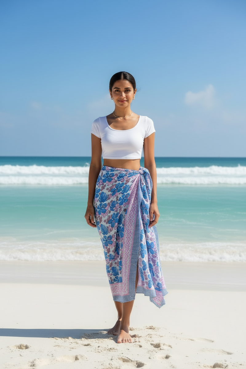 Woman standing on a beach wearing a white top and blue floral sarong.