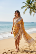 Woman in a yellow saree standing on a beach with palm trees in the background