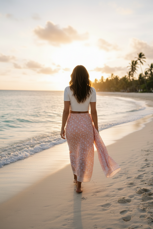 Woman walking on a beach at sunset with palm trees in the background