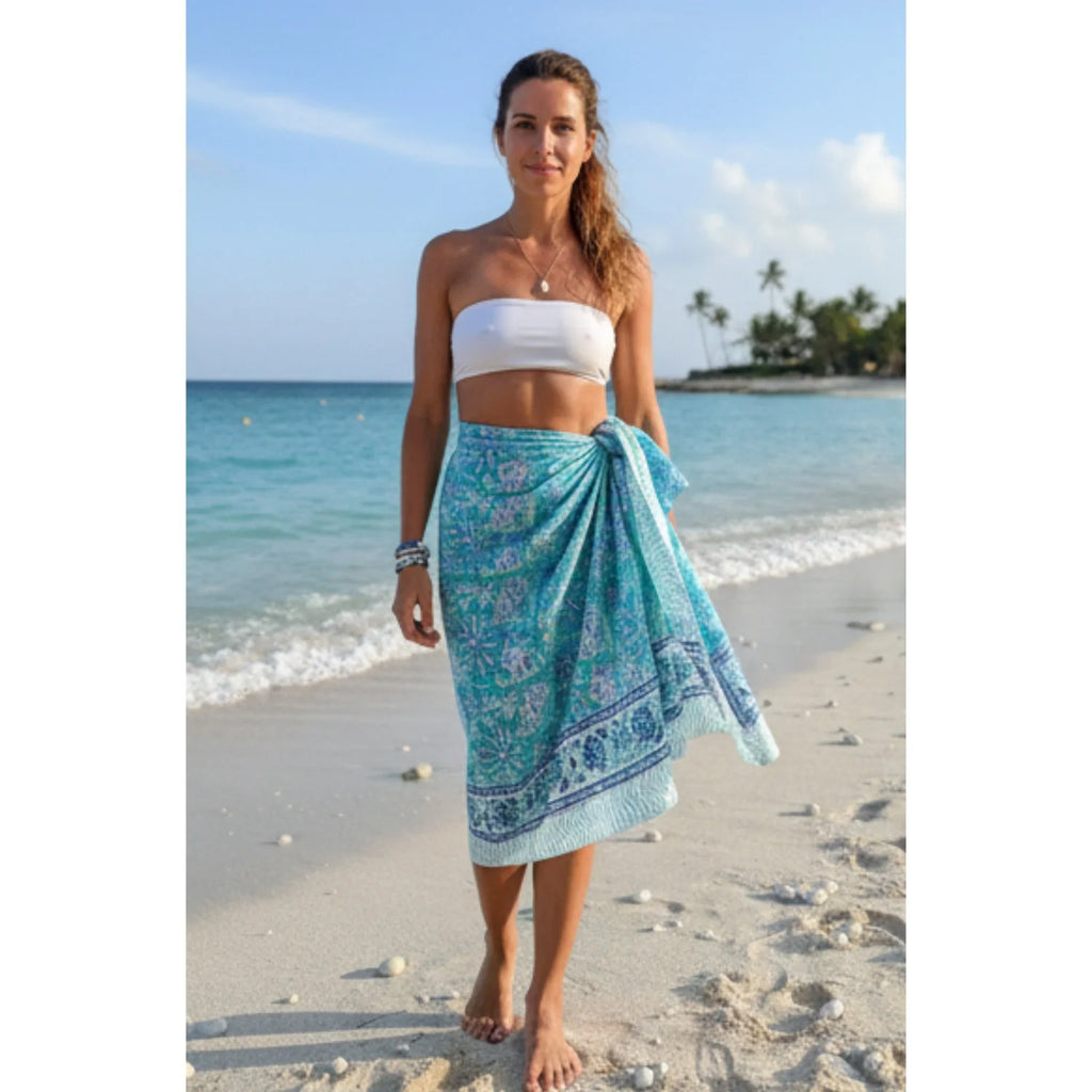 Woman on a beach wearing a white top and blue floral sarong